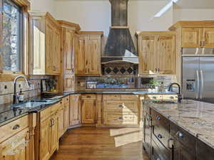 Kitchen featuring light stone countertops, built in refrigerator, sink, and wood-type flooring