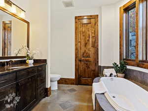 Bathroom with concrete flooring, vanity, toilet, and a bathing tub