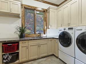 Clothes washing area featuring cabinets, separate washer and dryer, crown molding, and sink