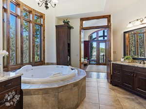 Bathroom featuring a chandelier, vanity, a relaxing tiled tub, and a wealth of natural light