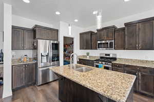 Kitchen with dark hardwood / wood-style flooring, dark brown cabinets, stainless steel appliances, sink, and a center island with sink