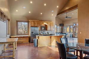 Kitchen with light stone countertops, stainless steel fridge, ceiling fan, high vaulted ceiling, and a breakfast bar area