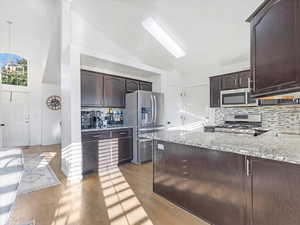 Kitchen with hardwood / wood-style floors, backsplash, high vaulted ceiling, appliances with stainless steel finishes, and decorative light fixtures