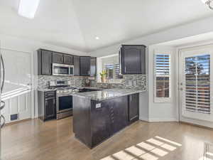 Kitchen with backsplash, kitchen peninsula, light stone counters, and stainless steel appliances