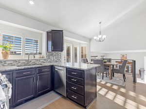 Kitchen with dishwasher, sink, light stone counters, kitchen peninsula, and hardwood / wood-style floors