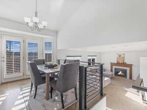 Dining space with a notable chandelier, light wood-type flooring, a fireplace, and vaulted ceiling