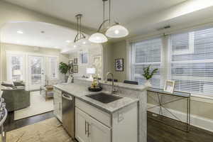 Kitchen featuring sink, dark wood-type flooring, light stone counters, pendant lighting, and white cabinets