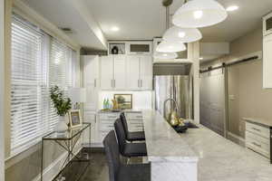 Kitchen featuring light stone countertops, a barn door, stainless steel fridge, and hanging light fixtures