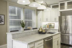 Kitchen with white cabinetry, sink, hanging light fixtures, stainless steel appliances, and an island with sink