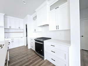 Kitchen featuring stainless steel gas stove, dark hardwood / wood-style flooring, white cabinetry, and tasteful backsplash