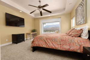 Carpeted bedroom featuring ceiling fan and a tray ceiling