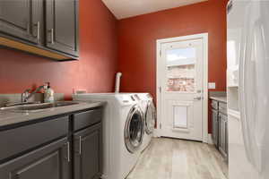 Washroom with washer and dryer, sink, cabinets, and light hardwood / wood-style flooring