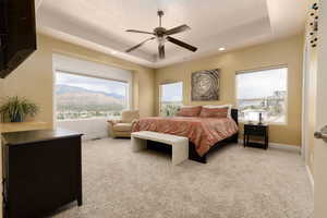 Bedroom with ceiling fan, a raised ceiling, light carpet, and multiple windows