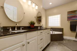 Bathroom with tile patterned flooring, vanity, and a relaxing tiled tub