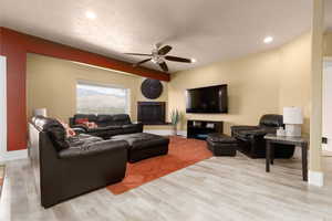 Living room with a textured ceiling, light wood-type flooring, and ceiling fan