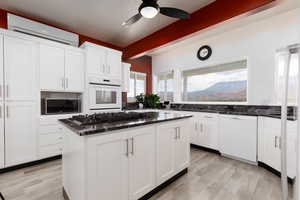 Kitchen featuring light wood-type flooring, white appliances, a wall mounted AC, a center island, and white cabinetry