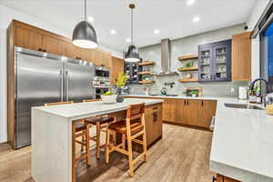 Kitchen with sink, built in appliances, light wood-type flooring, a kitchen island, and extractor fan