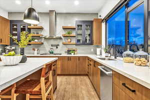 Kitchen featuring appliances with stainless steel finishes, light wood-type flooring, sink, decorative light fixtures, and range hood