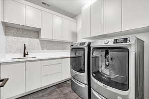 Clothes washing area with washer and clothes dryer, sink, cabinets, and dark tile patterned flooring