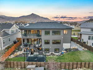 Back house at dusk with a lawn, a mountain view, a patio area, and a balcony