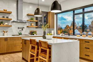 Kitchen with a center island, hanging light fixtures, wall chimney exhaust hood, light hardwood / wood-style floors, and a kitchen bar