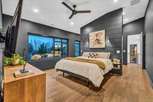 Bedroom with light hardwood / wood-style flooring, ceiling fan, lofted ceiling, and wood walls