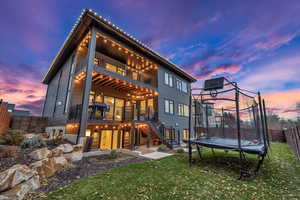 Back house at dusk with a balcony, a trampoline, a yard, and a deck