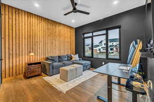 Living room with ceiling fan, wood walls, and wood-type flooring