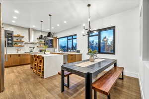 Kitchen featuring a center island, hanging light fixtures, light hardwood / wood-style flooring, wall chimney exhaust hood, and a breakfast bar area