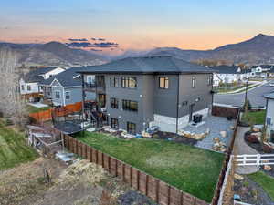 Back house at dusk with a mountain view, a yard, and a balcony