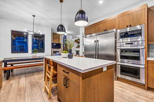 Kitchen with pendant lighting, light hardwood / wood-style floors, a kitchen island, and built in appliances