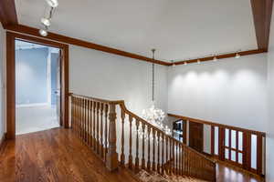 Staircase featuring wood-type flooring, ornamental molding, rail lighting, and a chandelier