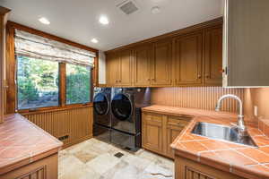 Laundry area featuring washer and clothes dryer, wooden walls, sink, and cabinets