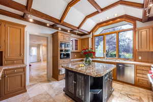 Kitchen with light stone countertops, a center island, sink, lofted ceiling, and appliances with stainless steel finishes