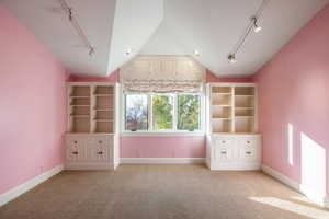 Unfurnished bedroom with rail lighting, light carpet, and vaulted ceiling