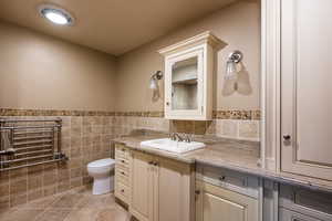 Bathroom featuring toilet, vanity, tile patterned floors, and tile walls