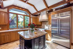 Kitchen with appliances with stainless steel finishes, premium range hood, sink, vaulted ceiling with beams, and a kitchen island