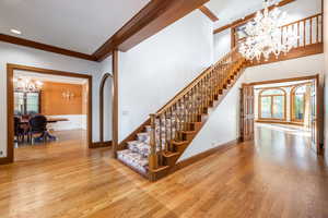 Stairs featuring wood-type flooring, an inviting chandelier, and crown molding