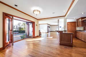 Kitchen featuring hardwood / wood-style flooring, crown molding, a center island with sink, and dark stone countertops