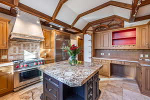 Kitchen featuring light stone countertops, a center island, backsplash, premium range hood, and high quality appliances