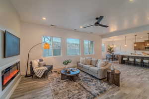 Living room with ceiling fan with notable chandelier and light hardwood / wood-style floors