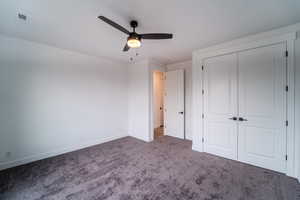 Unfurnished bedroom with ceiling fan, dark carpet, and a closet