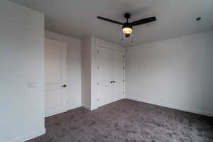 Unfurnished bedroom featuring ceiling fan, dark carpet, and a closet