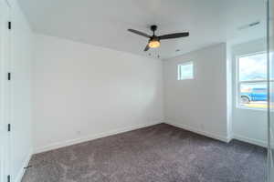 Empty room featuring ceiling fan and dark carpet