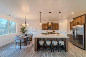 Kitchen featuring stainless steel appliances, an inviting chandelier, light wood-type flooring, hanging light fixtures, and a center island with sink