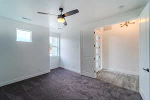 Spare room featuring ceiling fan with notable chandelier and dark carpet