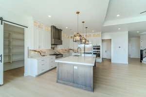 Kitchen featuring stainless steel appliances, a center island with sink, white cabinetry, hanging light fixtures, and a barn door