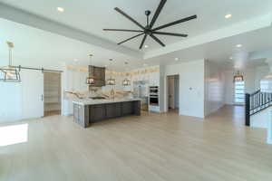 Kitchen with a barn door, a large island, decorative light fixtures, stainless steel refrigerator, and custom range hood