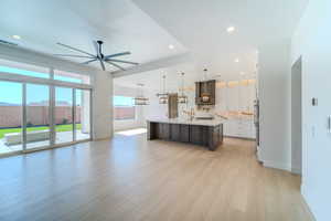 Kitchen with custom range hood, a spacious island, decorative light fixtures, and light hardwood / wood-style flooring