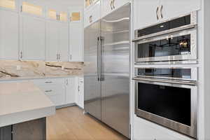 Kitchen with stainless steel appliances, white cabinets, light wood-style floors, glass insert cabinets, and tasteful backsplash